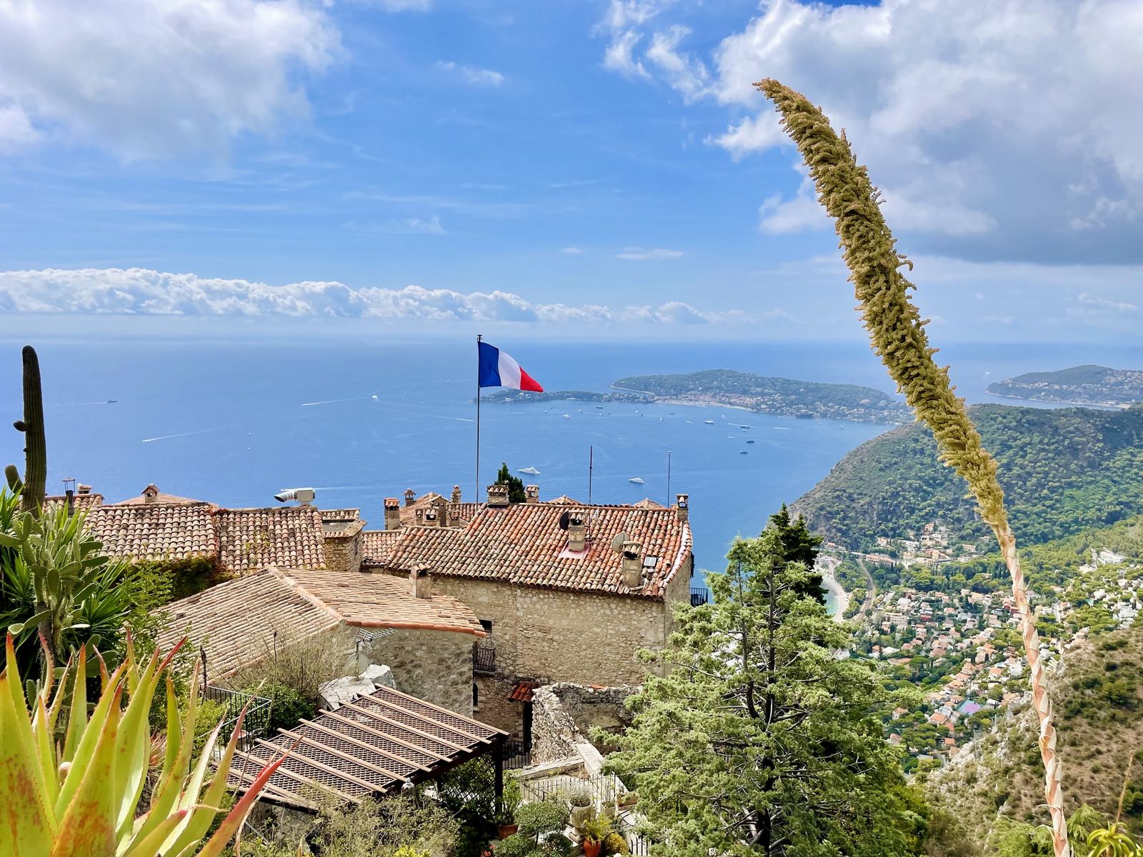 View from the very top of Eze — French flag, terracotta rooftops, the deep blue Mediterranean stretching to the horizon